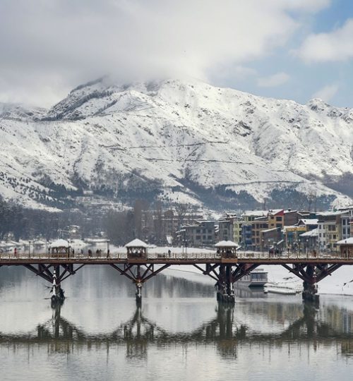 Srinagar: People walk across a footbridge as snowclad Zabarwan mountains are seen in the backdrop, after a heavy snowfall, in Srinagar, Wednesday, Jan. 6, 2021. (PTI Photo/S. Irfan)(PTI01_06_2021_000100A)